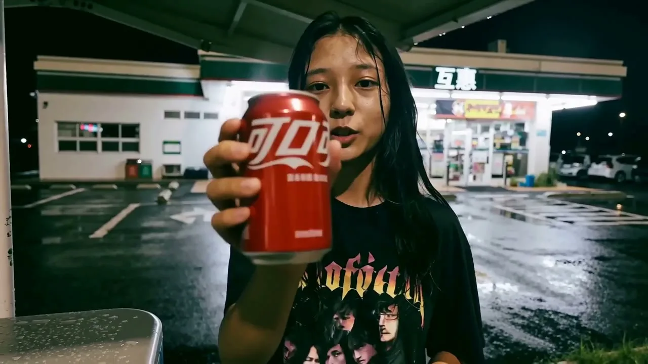 A girl holding a red can outside a convenience store at night
